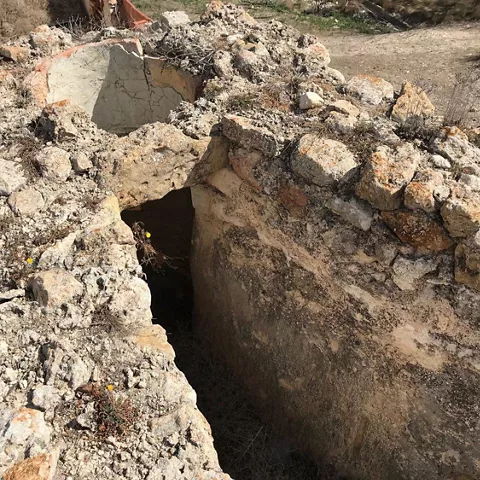 Restos de estructura de piedra con hueco profundo excavado en el suelo.