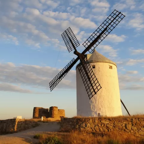 Molino de viento blanco iluminado por luz dorada junto a restos de muralla.