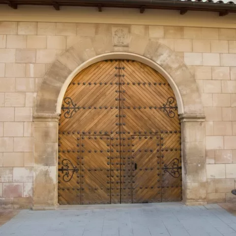Puerta de madera con clavos decorativos enmarcada por un arco de piedra.