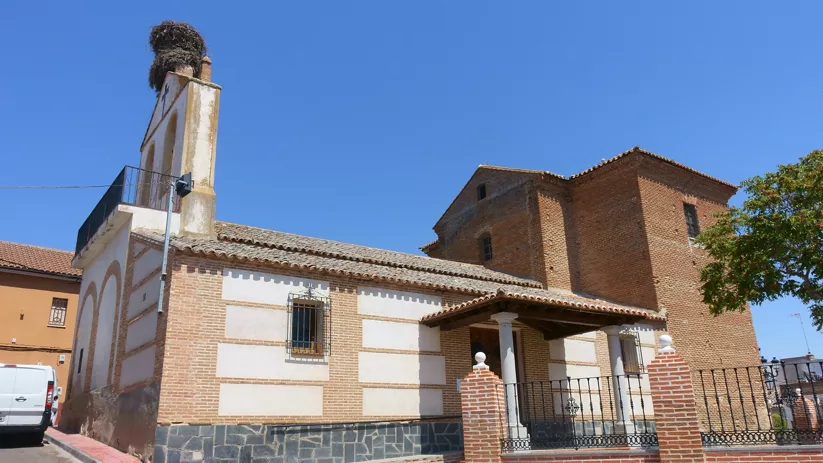 Iglesia de ladrillo y piedra con porche de entrada y espadaña con nido