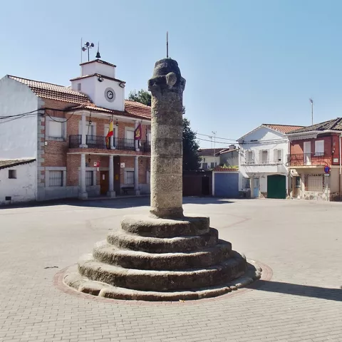 Plaza con columna de piedra en primer plano y edificio municipal al fondo