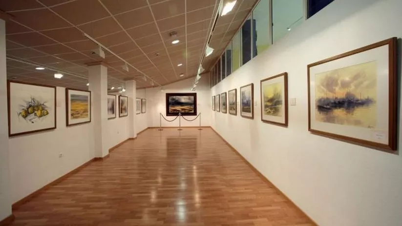 Pasillo expositivo con obras de arte alineadas en paredes blancas.