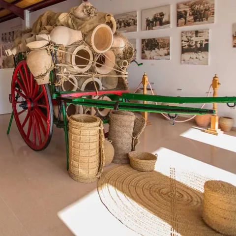 Interior de museo con carro tradicional cargado de cerámica y piezas artesanales.