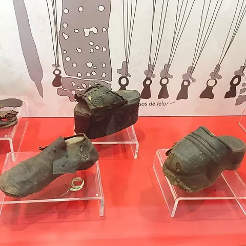 Calzado antiguo de cuero expuesto en vitrinas transparentes sobre fondo rojo.