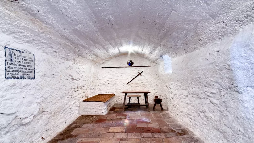 Estancia subterránea encalada con mesa y objetos históricos