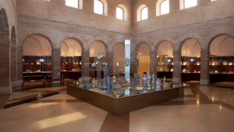 Patio interior con arcos y una vitrina central de cerámicas, rodeado de exposiciones.