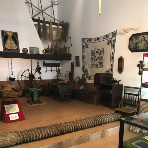 Interior con mobiliario rústico, telar y aperos colgados en la pared.