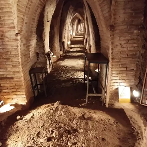 Pasillo abovedado de bodega excavada con iluminación cálida y suelo de tierra.