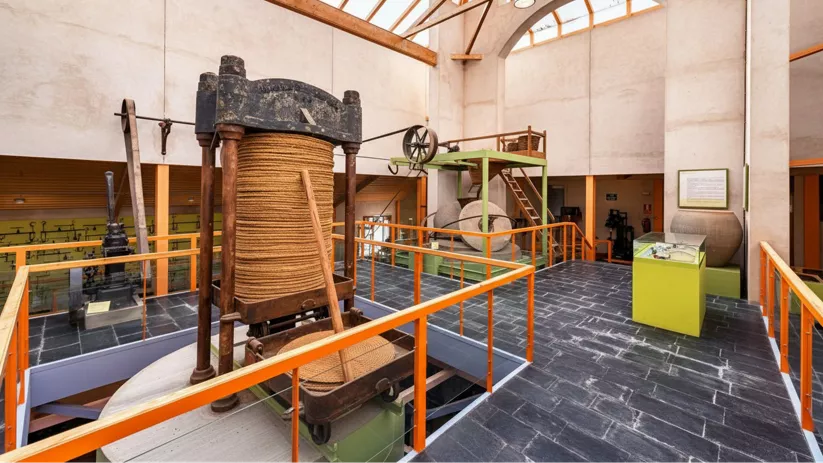 Planta superior de museo con maquinaria tradicional y estructura de vigas vistas.