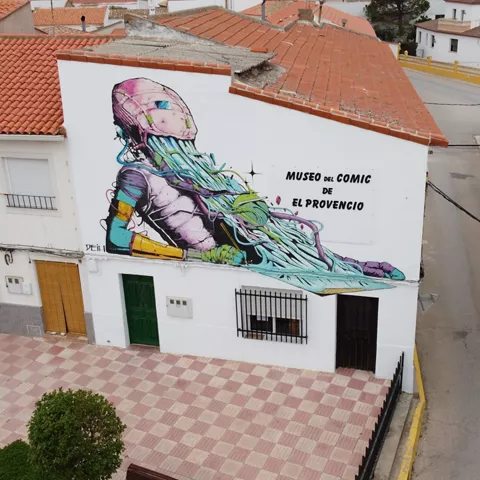 Fachada urbana con gran mural artístico en pared blanca.