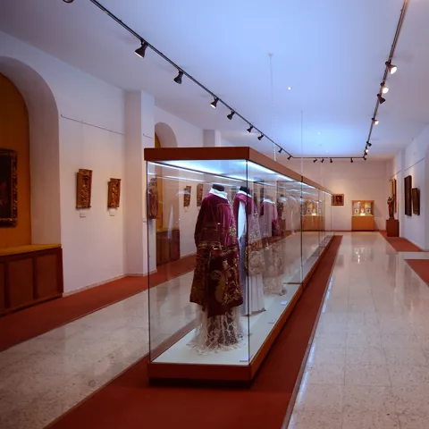 Galería de museo con vitrinas de vestimentas religiosas y obras de arte sacro