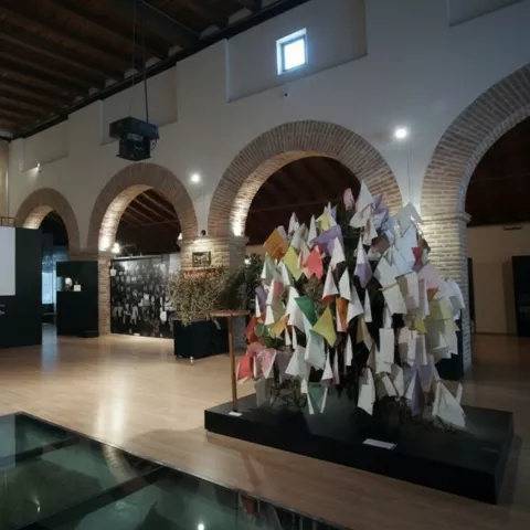 Espacio expositivo con arcos y una instalación de papeles colgantes en primer plano.