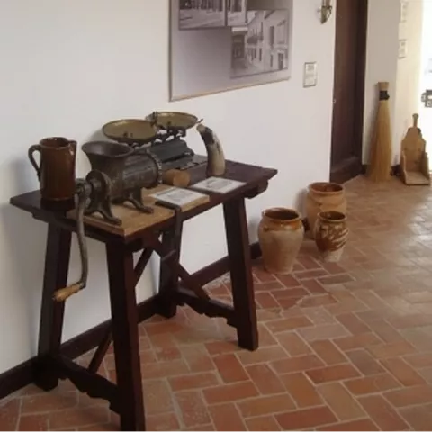 Rincón de exposición con mesa de madera y utensilios antiguos sobre suelo de ladrillo.