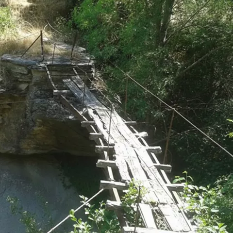 Pasarela de madera sobre cauce rocoso.