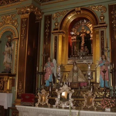 Retablo barroco con hornacina dorada, cruz central y figuras religiosas a los lados.