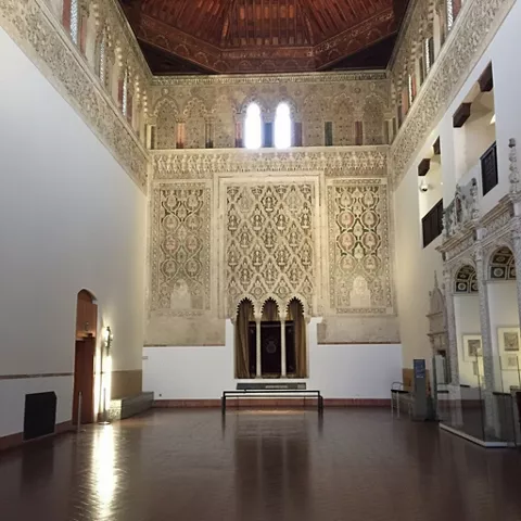 Gran sala interior con muros decorados, arcos y techo artesonado.