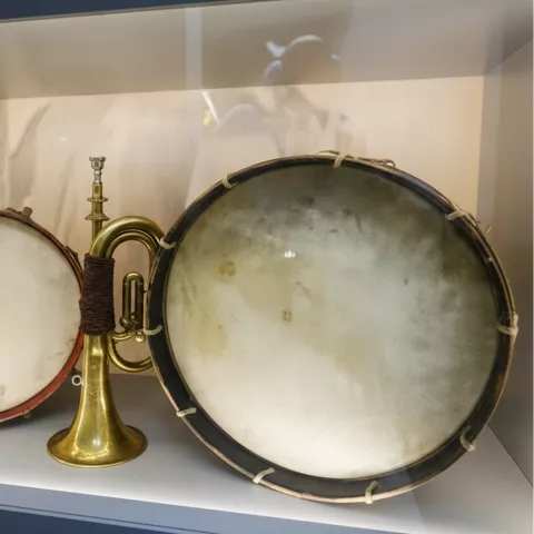 Instrumentos antiguos en vitrina: dos tambores y una trompeta de metal.