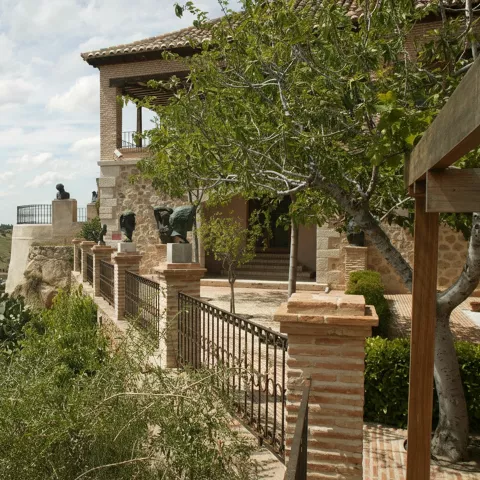 Casa de piedra con esculturas en la terraza y paisaje al fondo.