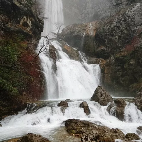 Cascadas escalonadas entre rocas y niebla, con agua blanca y árboles dispersos.