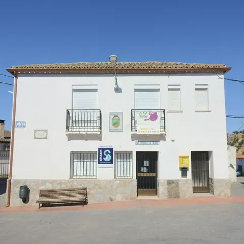 Edificio blanco de servicios públicos con carteles y banco