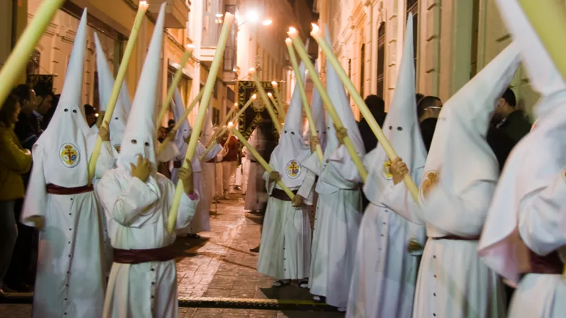 Nazarenos con túnicas blancas y cirios encendidos durante una procesión nocturna