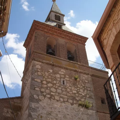 Torre campanario de piedra y ladrillo vista desde una calle estrecha