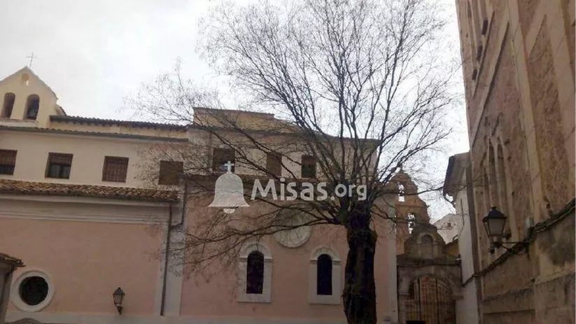 Vista exterior de un conjunto arquitectónico antiguo con árboles y campanario al fondo.