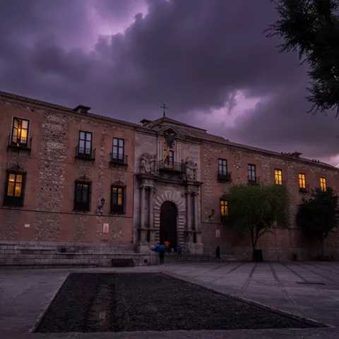 Edificio histórico iluminado al anochecer con cielo tormentoso.