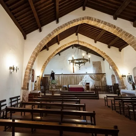 Interior de iglesia con bancos de madera, arcos de piedra y altar al fondo.