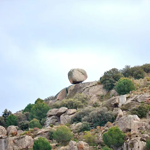 Gran roca equilibrada en ladera con matorral