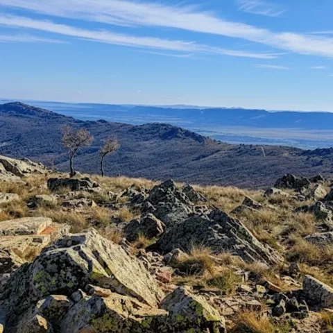 Cumbre rocosa con matorrales y sierras onduladas en el horizonte.