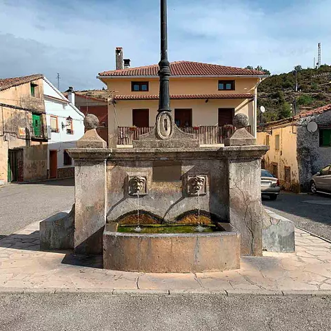Fuente de piedra en una plaza con viviendas tradicionales alrededor.