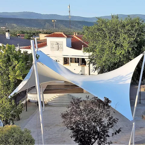 Plaza con escenario cubierto por lonas blancas y árboles alrededor.