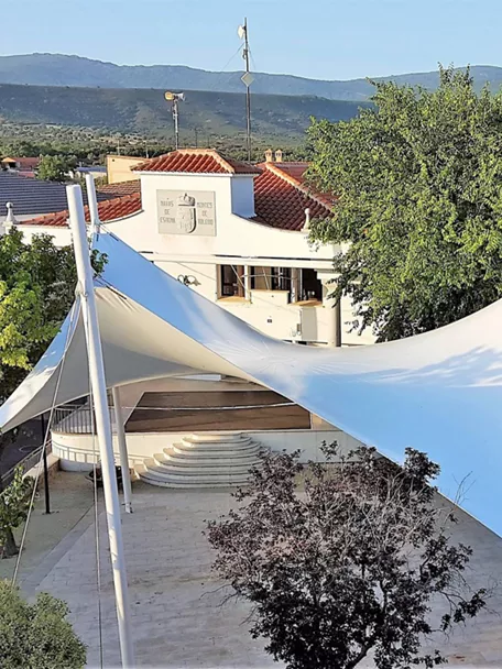 Plaza con escenario cubierto por lonas blancas y árboles alrededor.