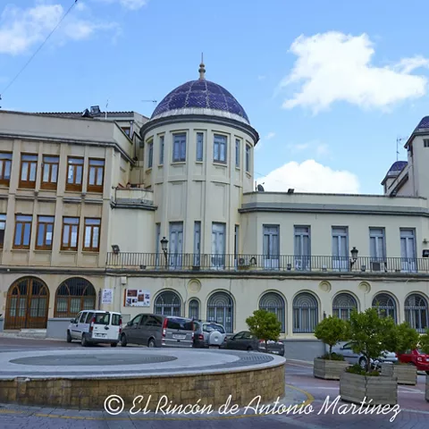 Fachada monumental con cúpulas cerámicas azules, arcos en planta baja y plaza pavimentada delante.