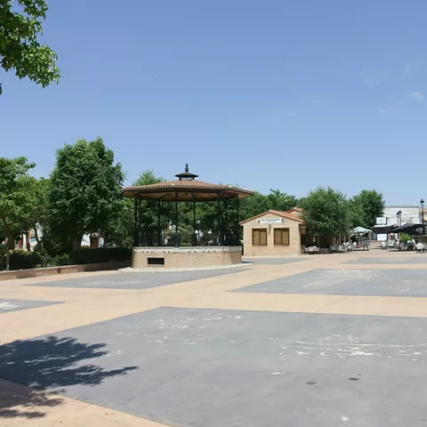 Plaza abierta con quiosco central y arbolado           