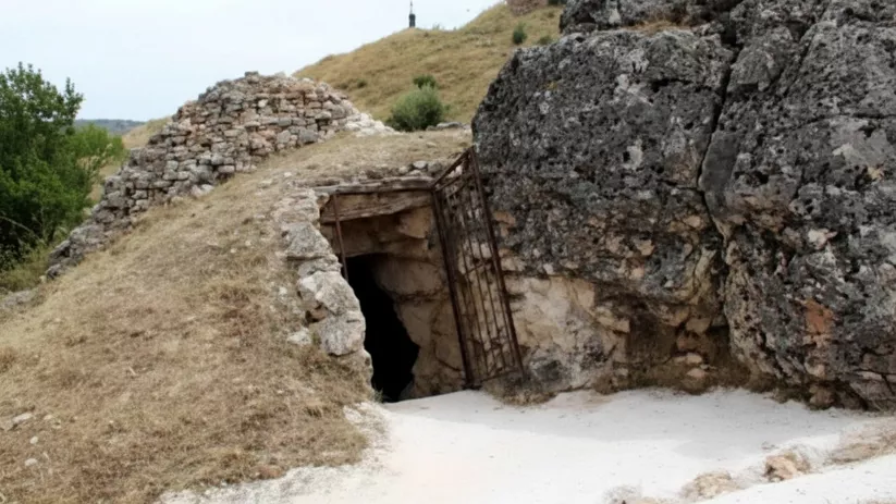 Entrada excavada en roca con puerta de hierro.
