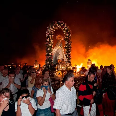 Multitud caminando junto a hogueras encendidas de noche.