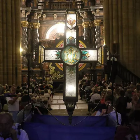 Cruz luminosa en el interior de un templo abarrotado.