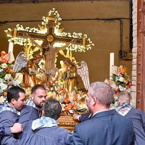 Costaleros portando un paso con una figura crucificada adornada con flores.