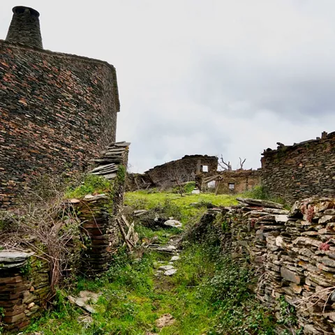 Callejuela de piedra entre muros y ruinas cubiertas de vegetación.