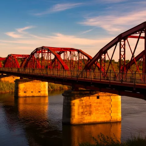 Puente rojo iluminado por el atardecer, reflejado en el río.