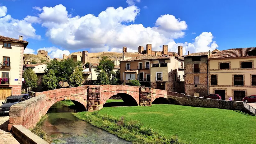Puente medieval de tres arcos sobre río.