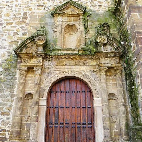 Portada monumental de piedra con arco decorado y puerta de madera.