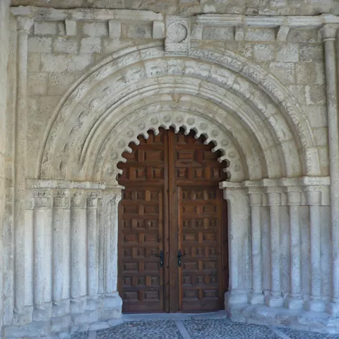 Portada románica con arco decorado y puerta de madera.