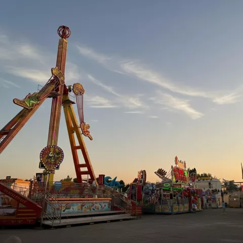 Atracciones de feria al atardecer en una plaza casi vacía.