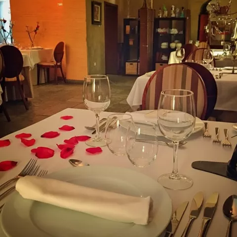 Mesa de restaurante preparada con copas, cubiertos y pétalos de rosa.