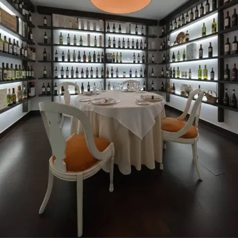 Comedor privado con mesa redonda y lámpara grande, rodeado de estantes con botellas.