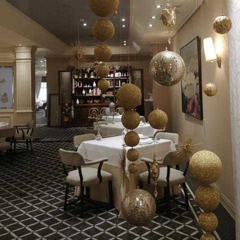 Salón decorado con esferas colgantes doradas y mesas redondas vestidas.