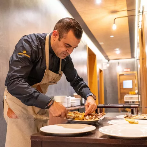 Cocinero emplatando comida en una mesa de servicio.